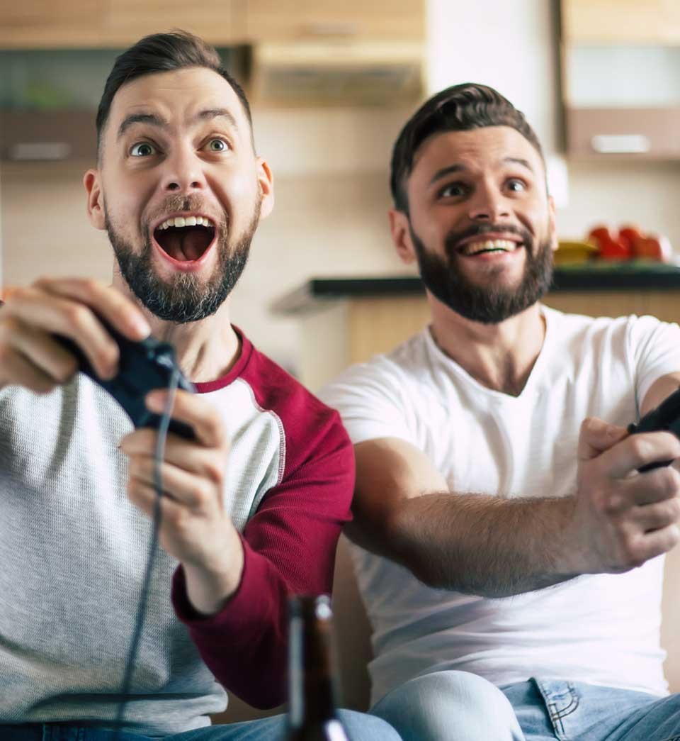 Excited smiling men playing in video games on tv at home on the couch. Friends with joysticks play game with happy emotions on faces Excited smiling men playing in video games on tv at home on the couch. Friends with joysticks play game with happy emotions on faces