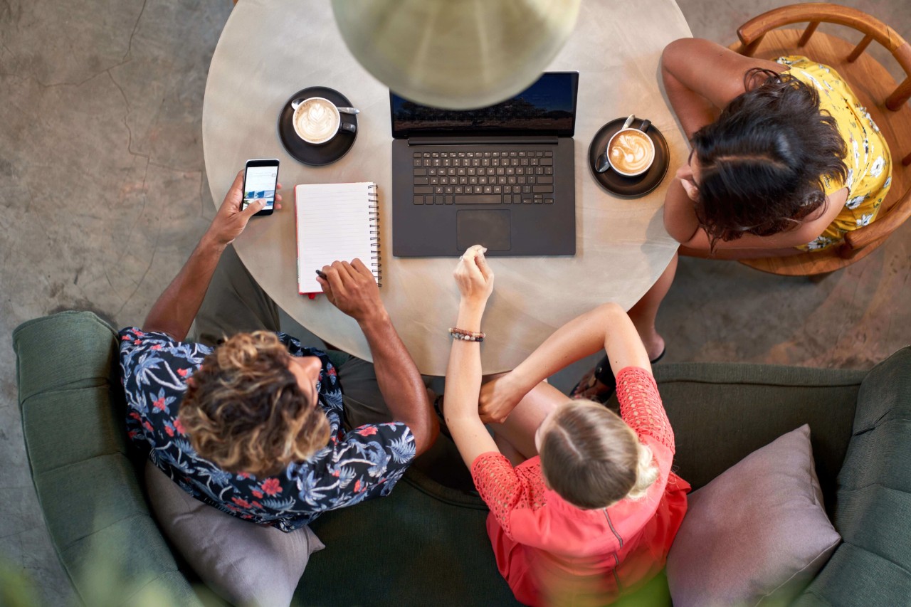 Overhead shot of three people collaborating over coffee with a laptop at a café Overhead shot of three people collaborating over coffee with a laptop at a café