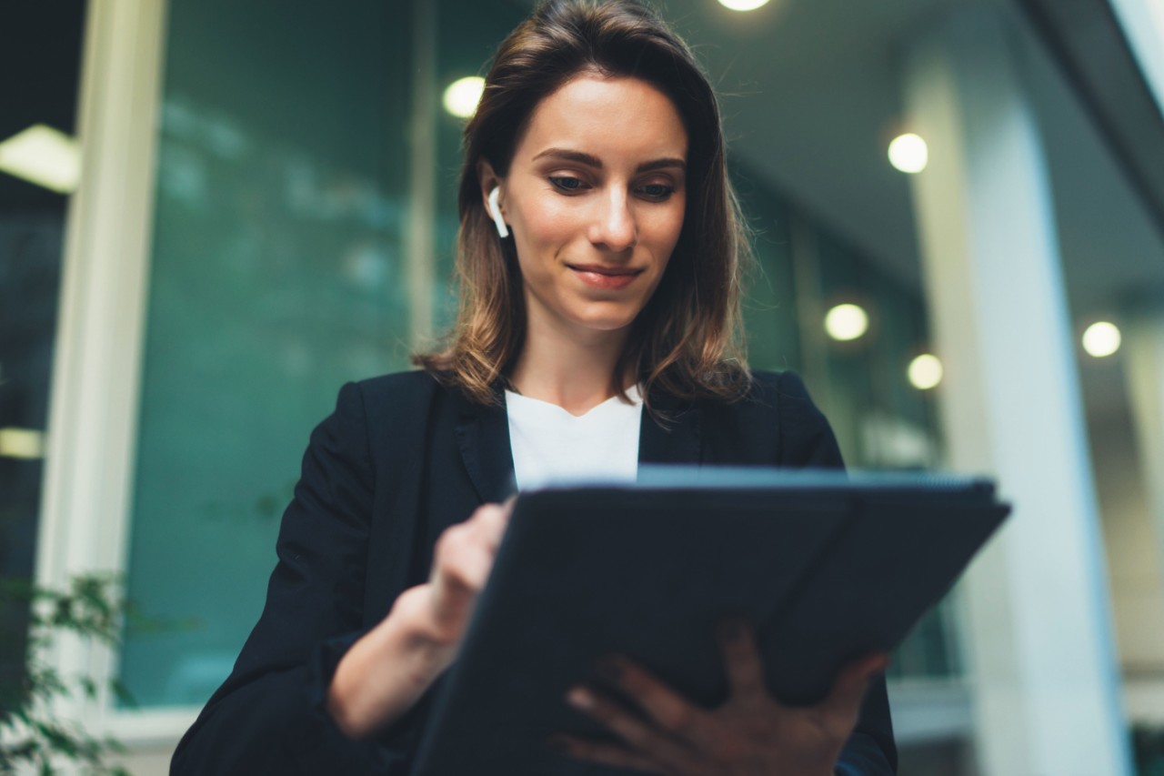 Woman using a tablet and wireless earphones outdoors with office background lights