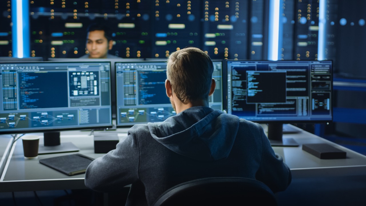 Team of network security managers looking at network threat data on multiple screens Team of network security managers looking at network threat data on multiple screens