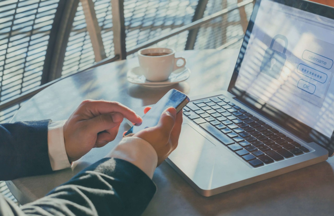 hands holding a smart phone in front a laptop using two-factor authentication hands holding a smart phone in front a laptop using two-factor authentication